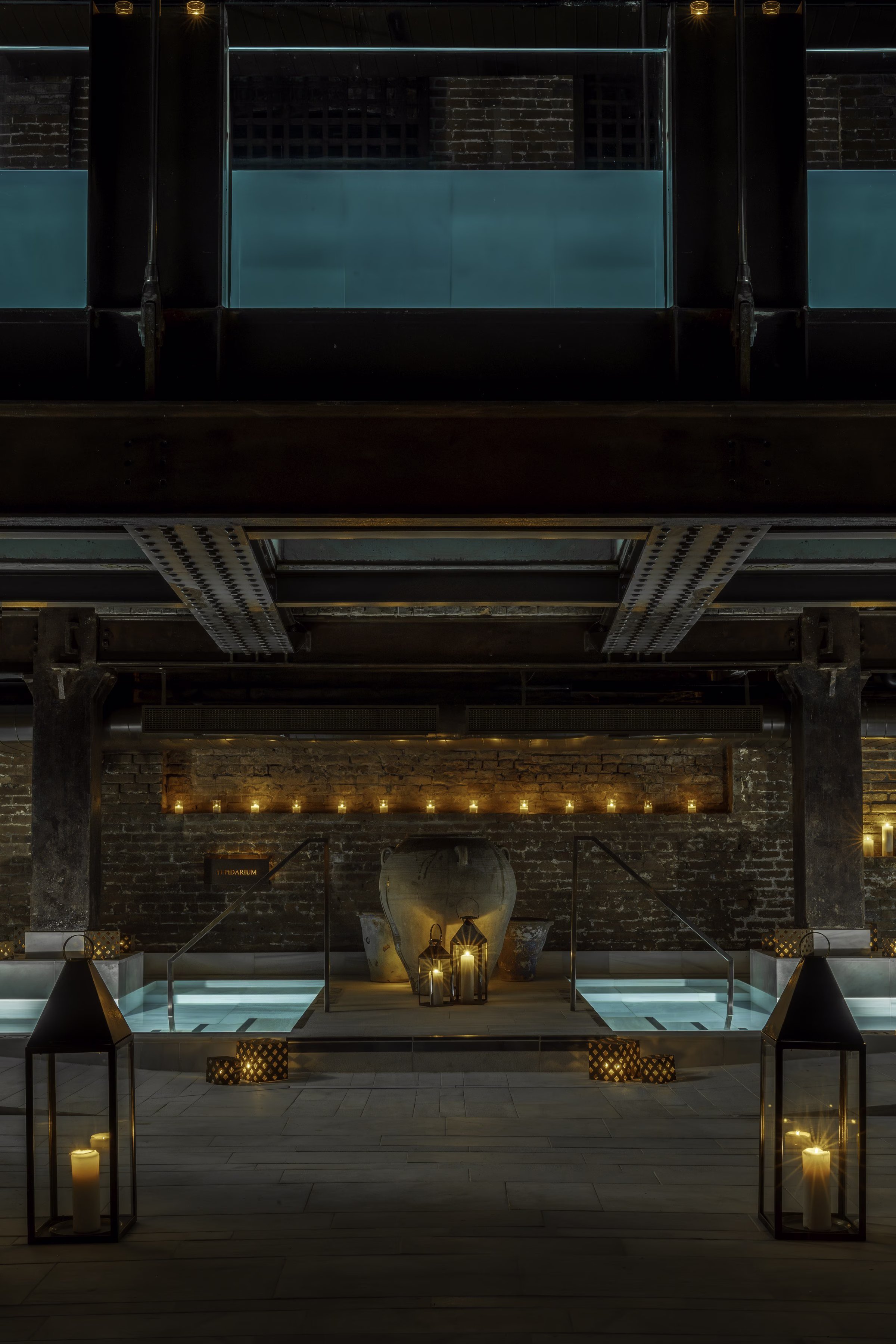AIRE Ancient Baths Tribeca Tepidarium with sculptural amphora and candlelit lanterns beneath industrial beams