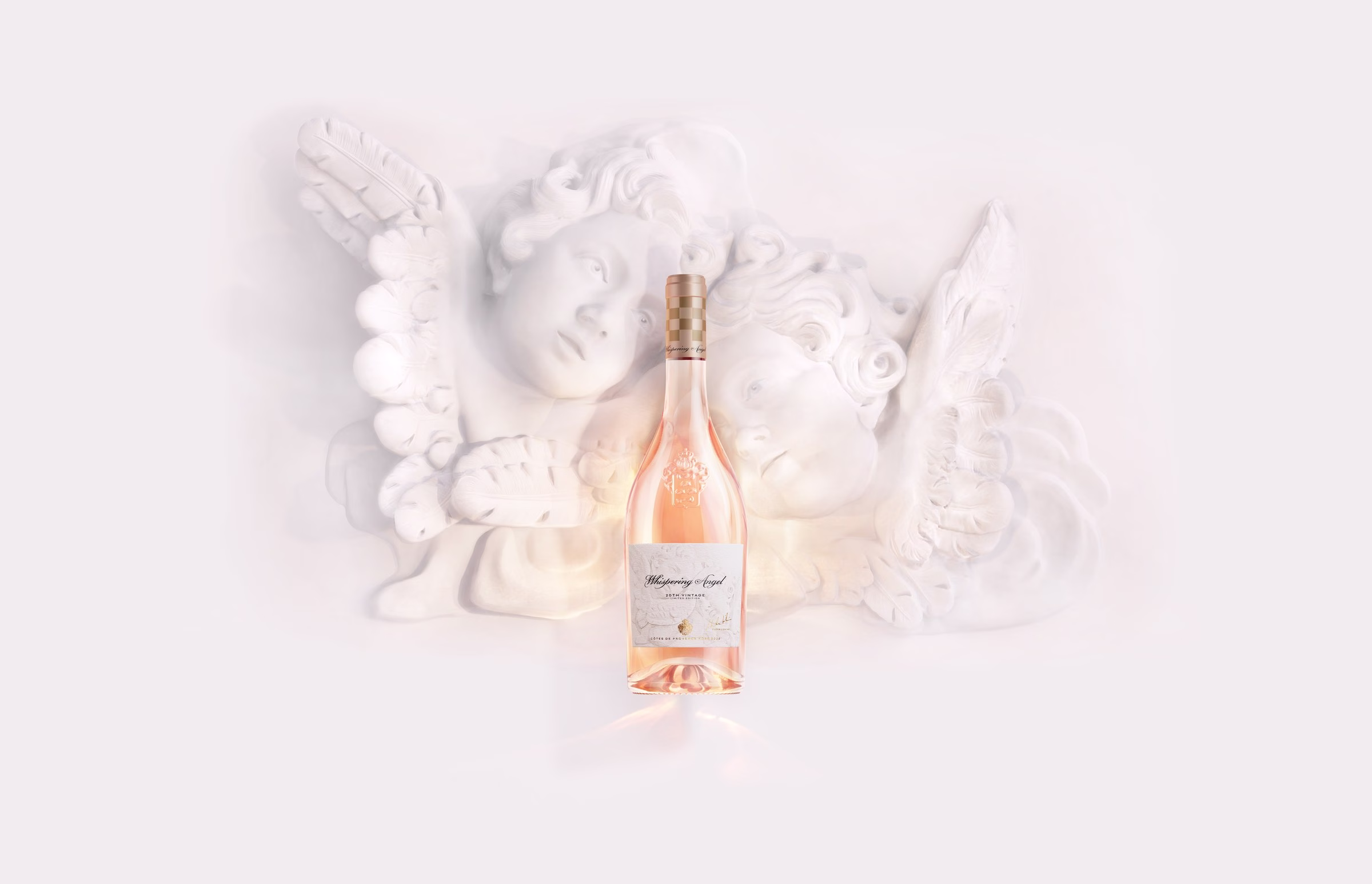 Chateau d'Esclans Whispering Angel 20th Anniversary limited-edition rosé bottle backlit beside sculptural marble cherubs