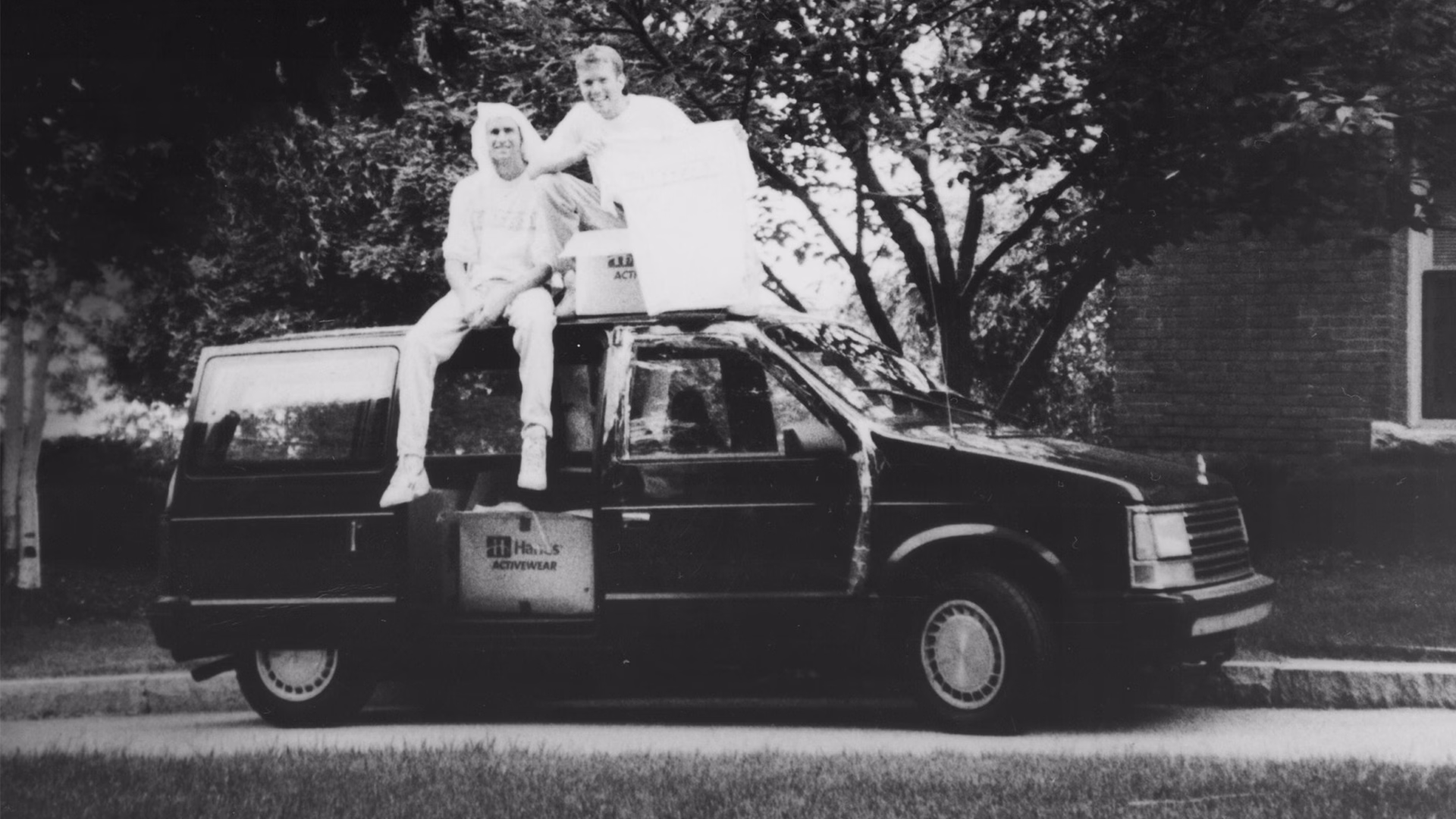 Life is Good founders John and Bert Jacobs sitting atop their early sales van in a vintage black-and-white archive photo