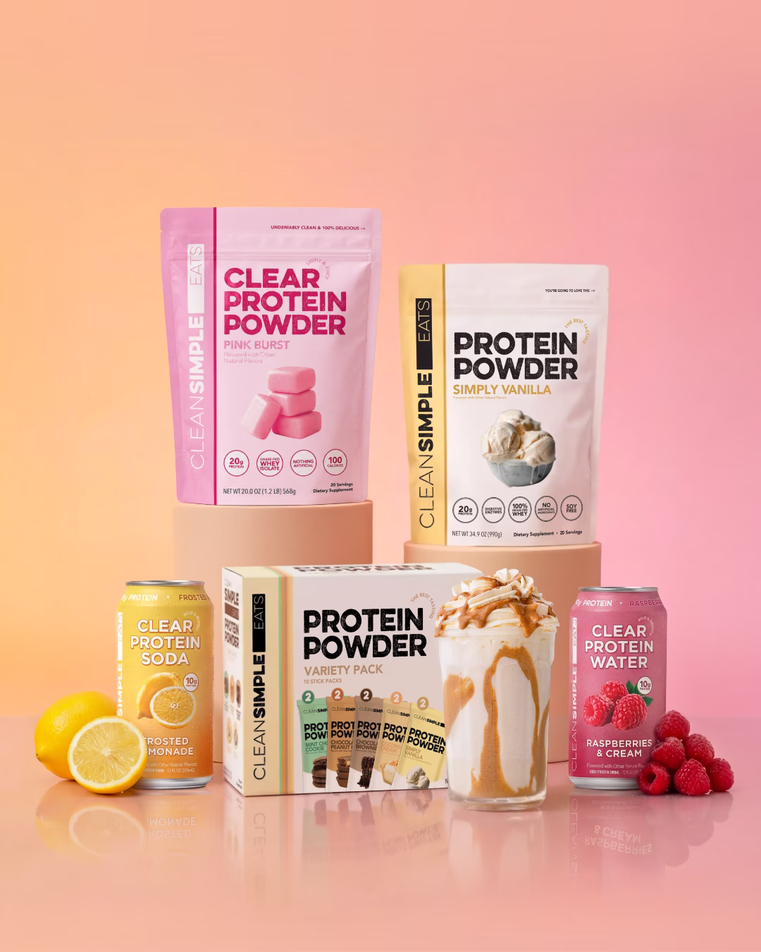 Clean Simple Eats protein product lineup featuring Clear Protein Powder in Pink Burst, Simply Vanilla Protein Powder, Protein Powder Variety Pack, Clear Protein Soda in Frosted Monade, and Clear Protein Water in Raspberries and Cream flavor, styled against a warm peach and pink gradient background
