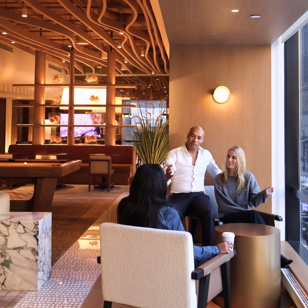Three colleagues having a casual coffee meeting in the modern warm-toned lobby lounge of M Social Hotel New York Downtown in the Financial District