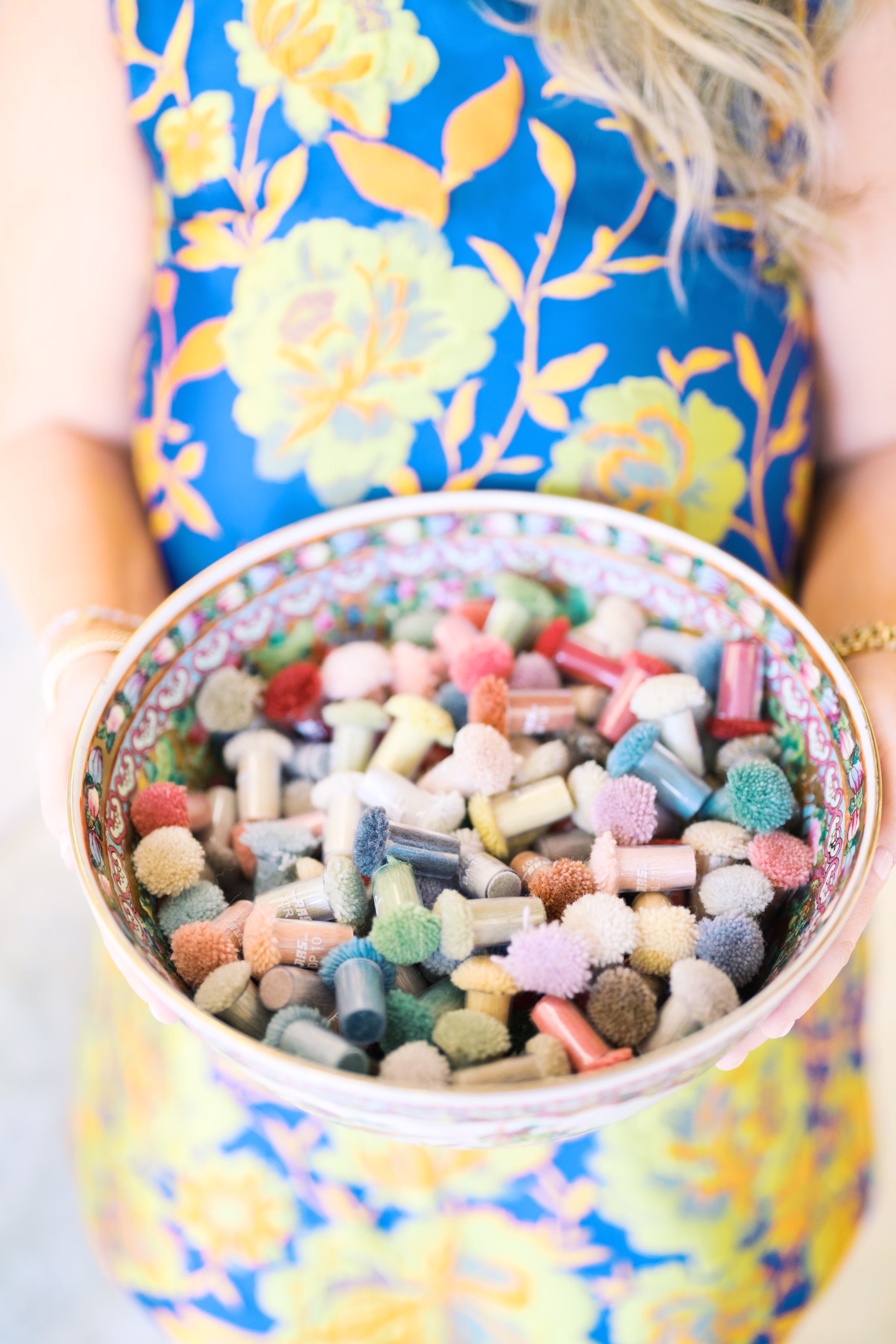 colorful textile samples bowl dfw textile sourcing - Magrino welcomes DFW Textile Sourcing and Serefina Studio to its roster Person in blue floral dress holding a decorative porcelain bowl filled with colorful fabric and carpet sample swatches from DFW Textile Sourcing